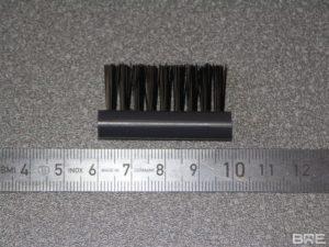 Une brosse d'étiqueteuse industrielle fixée sur un bras mécanique. Les poils en nylon souples de la brosse retiennent l'étiquette pendant l'échenillage pour un placement précis et une application uniforme.