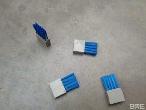 Une brosse industrielle en fibres synthétiques fixée sur un support métallique, utilisée pour le pressage et le lissage des étiquettes sur des produits dans une chaîne d'étiquetage industrielle.